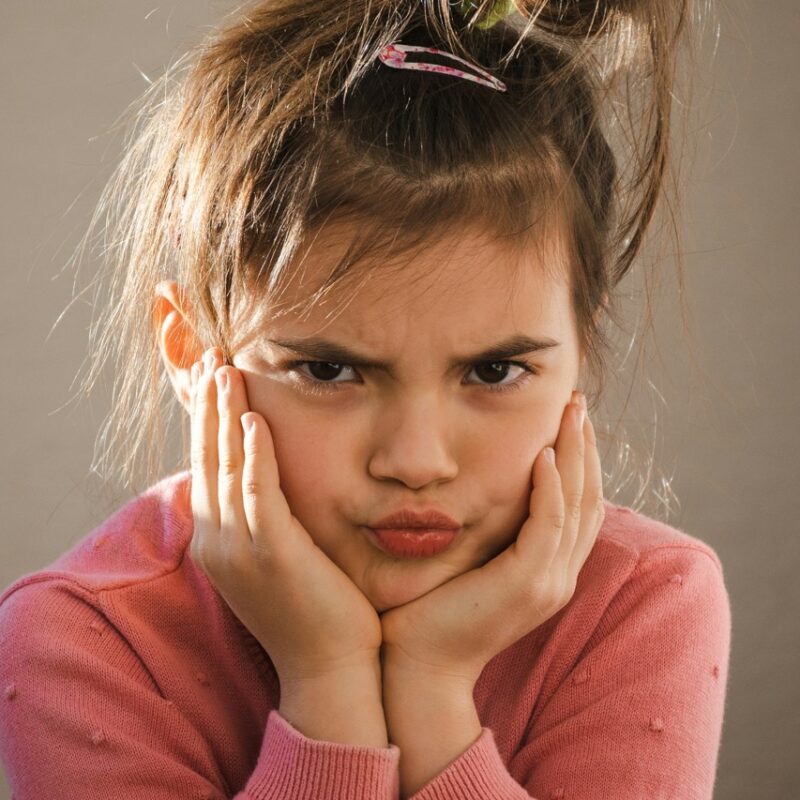 young girl holding face in hands looking angry having meltdown
