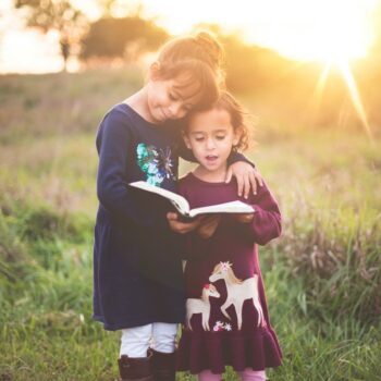two young girls reading a book in a field