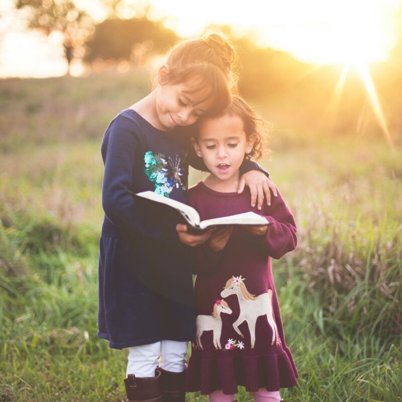 two young girls reading a book in a field